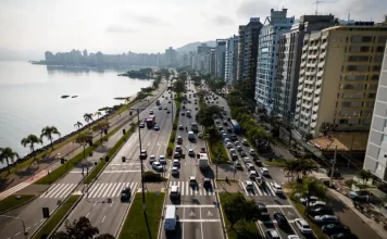 Florianópolis envia à Câmara projeto de nova regulamentação do transporte por aplicativos Vista aérea de uma avenida à beira-mar em Florianópolis com intenso fluxo de veículos e prédios residenciais ao lado. A imagem ilustra o contexto da mobilidade urbana na Capital e acompanha matéria sobre projeto de lei que atualiza as regras do transporte por aplicativos para ampliar segurança, fiscalização e qualidade do serviço.