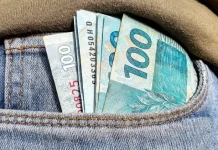 Foto do bolso de uma calça com notas de R$ 100,00 simbolizando a distribuição dos lucros do FGTS