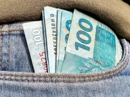Foto do bolso de uma calça com notas de R$ 100,00 simbolizando a distribuição dos lucros do FGTS