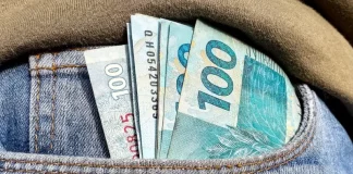Foto do bolso de uma calça com notas de R$ 100,00 simbolizando a distribuição dos lucros do FGTS