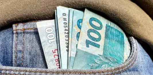 Foto do bolso de uma calça com notas de R$ 100,00 simbolizando a distribuição dos lucros do FGTS