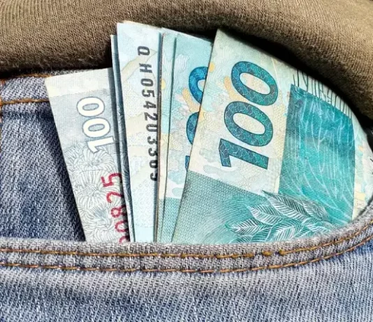Foto do bolso de uma calça com notas de R$ 100,00 simbolizando a distribuição dos lucros do FGTS