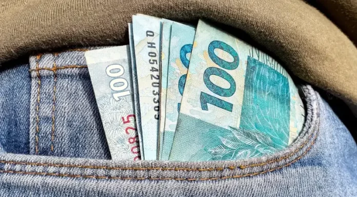 Foto do bolso de uma calça com notas de R$ 100,00 simbolizando a distribuição dos lucros do FGTS