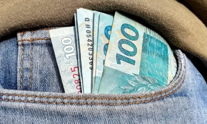Foto do bolso de uma calça com notas de R$ 100,00 simbolizando a distribuição dos lucros do FGTS