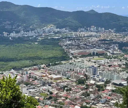 Vista panorâmica de Florianópolis mostra áreas urbanizadas, vegetação preservada e bairros da Capital, ilustrando o crescimento urbano e o planejamento territorial previsto no Plano Diretor.