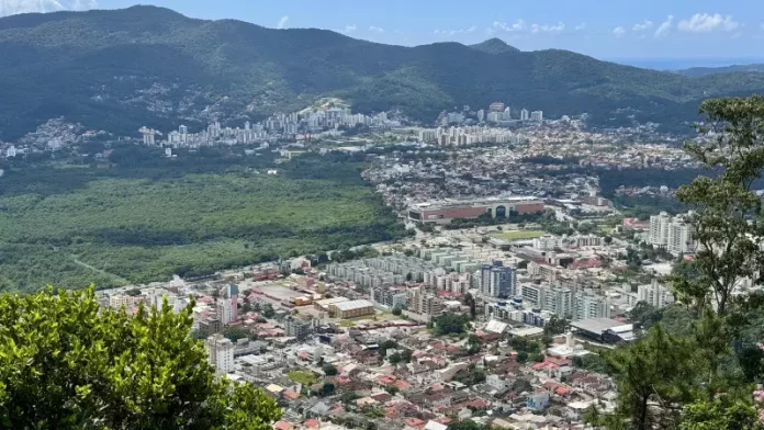 Vista panorâmica de Florianópolis mostra áreas urbanizadas, vegetação preservada e bairros da Capital, ilustrando o crescimento urbano e o planejamento territorial previsto no Plano Diretor.
