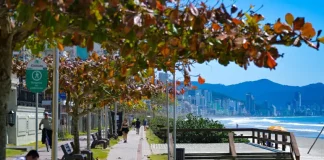 Pessoas caminham e pedalam no calçadão à beira-mar em dia de sol em Santa Catarina, ilustrando o contraste entre as manhãs de frio intenso e a elevação das temperaturas prevista para os próximos dias.