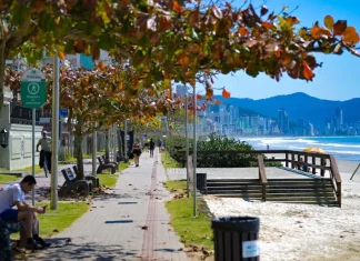 Pessoas caminham e pedalam no calçadão à beira-mar em dia de sol em Santa Catarina, ilustrando o contraste entre as manhãs de frio intenso e a elevação das temperaturas prevista para os próximos dias.