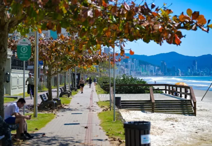 frio-perde-força Pessoas caminham e pedalam no calçadão à beira-mar em dia de sol em Santa Catarina, ilustrando o contraste entre as manhãs de frio intenso e a elevação das temperaturas prevista para os próximos dias.