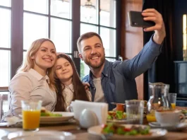 Foto de pai, mãe e filha, em restaurante, fazendo uma selfie, simbolizando almoço em família no Dia dos Pais