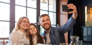 Foto de pai, mãe e filha, em restaurante, fazendo uma selfie, simbolizando almoço em família no Dia dos Pais