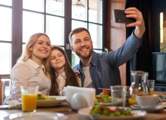 Dia dos Pais deve impulsionar vendas em bares e restaurantes Foto de pai, mãe e filha, em restaurante, fazendo uma selfie, simbolizando almoço em família no Dia dos Pais