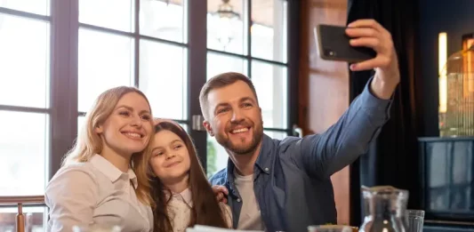 Dia dos Pais deve impulsionar vendas em bares e restaurantes Foto de pai, mãe e filha, em restaurante, fazendo uma selfie, simbolizando almoço em família no Dia dos Pais