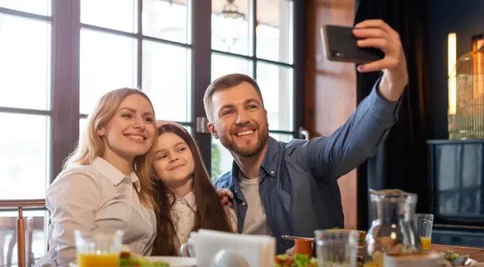 Foto de pai, mãe e filha, em restaurante, fazendo uma selfie, simbolizando almoço em família no Dia dos Pais