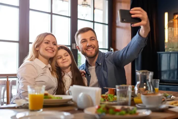 dia-dos-pais-abrasel Foto de pai, mãe e filha, em restaurante, fazendo uma selfie, simbolizando almoço em família no Dia dos Pais