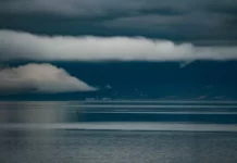 Foto do mar sob céu carregado de nuvens escuras e tempestade, com montanhas ao fundo, ilustrando a previsão do Fórum Climático de chuva acima da média e maior frequência de tempestades severas em Santa Catarina.