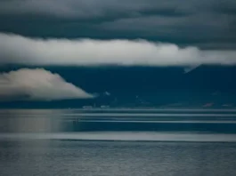 Foto do mar sob céu carregado de nuvens escuras e tempestade, com montanhas ao fundo, ilustrando a previsão do Fórum Climático de chuva acima da média e maior frequência de tempestades severas em Santa Catarina.