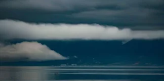 Foto do mar sob céu carregado de nuvens escuras e tempestade, com montanhas ao fundo, ilustrando a previsão do Fórum Climático de chuva acima da média e maior frequência de tempestades severas em Santa Catarina.