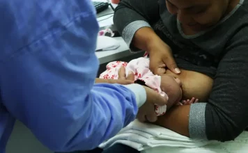 Foto de mãe amamentando criança com auxilio de enfermeira, simbolizando o curso de amamentação dutrante agosto dourado