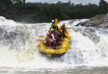 Grupo de pessoas pratica rafting em um rio de águas agitadas, descendo uma forte corredeira em meio à natureza, para ilustrar uma atividade de turismo de aventura.