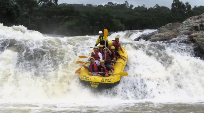 Grupo de pessoas pratica rafting em um rio de águas agitadas, descendo uma forte corredeira em meio à natureza, para ilustrar uma atividade de turismo de aventura.