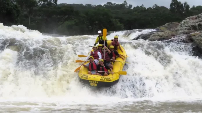 Grupo de pessoas pratica rafting em um rio de águas agitadas, descendo uma forte corredeira em meio à natureza, para ilustrar uma atividade de turismo de aventura.