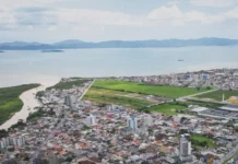 População de Biguaçu chega a 85.472 habitantes, aponta IBGE Vista aérea de Biguaçu mostra a área urbana do município, com prédios, casas, vias e a Baía Norte ao fundo, ilustrando a cidade que chegou a 85.472 habitantes em 2026.
