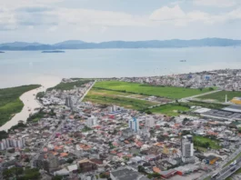 População de Biguaçu chega a 85.472 habitantes, aponta IBGE Vista aérea de Biguaçu mostra a área urbana do município, com prédios, casas, vias e a Baía Norte ao fundo, ilustrando a cidade que chegou a 85.472 habitantes em 2026.