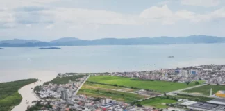 Vista aérea de Biguaçu mostra a área urbana do município, com prédios, casas, vias e a Baía Norte ao fundo, ilustrando a cidade que chegou a 85.472 habitantes em 2026.