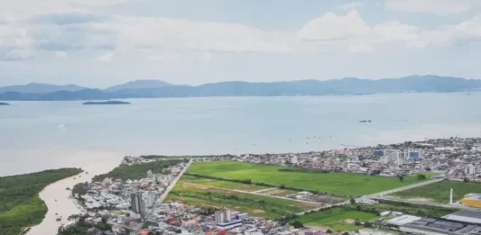 População de Biguaçu chega a 85.472 habitantes, aponta IBGE Vista aérea de Biguaçu mostra a área urbana do município, com prédios, casas, vias e a Baía Norte ao fundo, ilustrando a cidade que chegou a 85.472 habitantes em 2026.