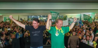 Flávio Bolsonaro e Jorginho Mello aparecem de mãos levantadas diante de apoiadores durante ato de campanha em Santa Catarina.