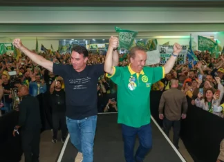 Flávio Bolsonaro e Jorginho Mello aparecem de mãos levantadas diante de apoiadores durante ato de campanha em Santa Catarina.