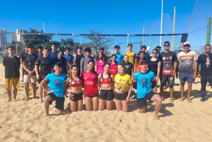 Projeto de vôlei de praia SJ Jovens atletas e treinadores do projeto de vôlei de praia de São José posam em quadra de areia, representando a formação esportiva e o desenvolvimento de novos talentos no município.