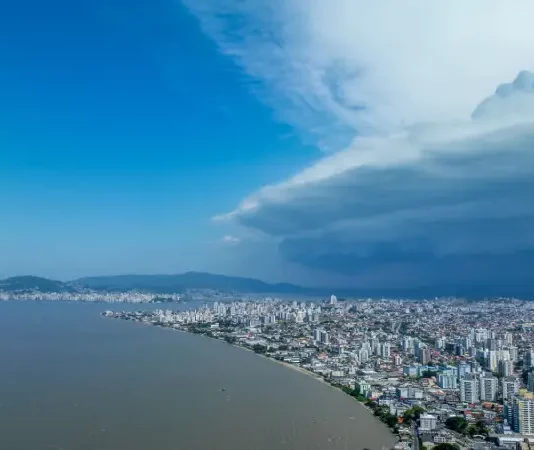Nuvens escuras de tempestade avançam sobre área urbana de Santa Catarina, imagem que ilustra o aumento do risco de temporais no estado.