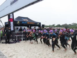 Atletas participam da largada do IRONMAN 70.3 em Florianópolis, acompanhados pelo público na praia.