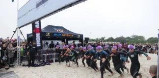 Atletas participam da largada do IRONMAN 70.3 em Florianópolis, acompanhados pelo público na praia.