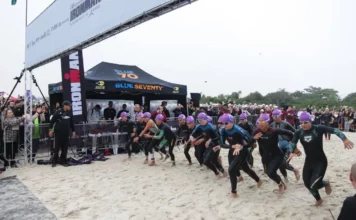 Atletas participam da largada do IRONMAN 70.3 em Florianópolis, acompanhados pelo público na praia.