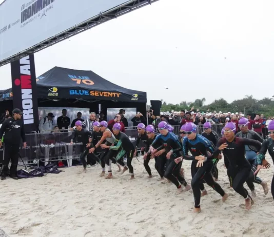 Atletas participam da largada do IRONMAN 70.3 em Florianópolis, acompanhados pelo público na praia.