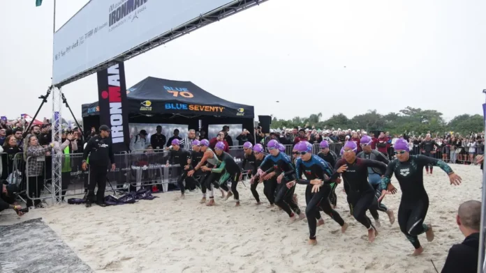 Atletas participam da largada do IRONMAN 70.3 em Florianópolis, acompanhados pelo público na praia.