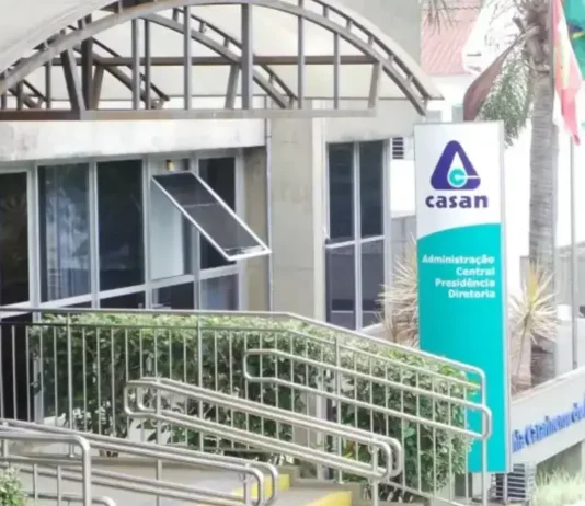Fachada da sede administrativa da Casan, em Florianópolis, com entrada de vidro, rampa de acesso e placa de identificação da companhia