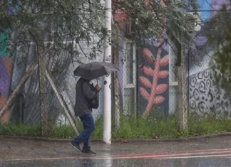 Pessoa caminha com guarda-chuva durante chuva intensa em Santa Catarina, onde a passagem de uma frente fria aumenta o risco de alagamentos e temporais.