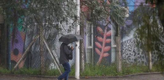 Pessoa caminha com guarda-chuva durante chuva intensa em Santa Catarina, onde a passagem de uma frente fria aumenta o risco de alagamentos e temporais.