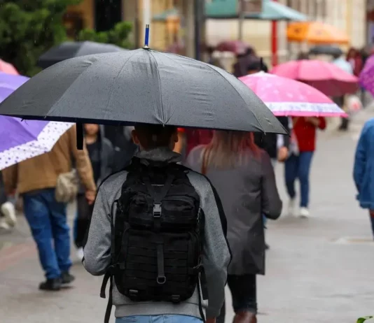 Pessoas caminham com guarda-chuvas durante chuva, imagem que ilustra a previsão de tempo instável em Santa Catarina.