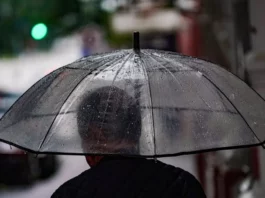 Pessoa caminha com guarda-chuva em rua molhada, ilustrando a previsão de chuva e temporais em Santa Catarina.