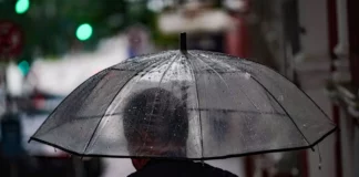 Pessoa caminha com guarda-chuva em rua molhada, ilustrando a previsão de chuva e temporais em Santa Catarina.