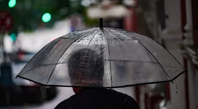 Pessoa caminha com guarda-chuva em rua molhada, ilustrando a previsão de chuva e temporais em Santa Catarina.