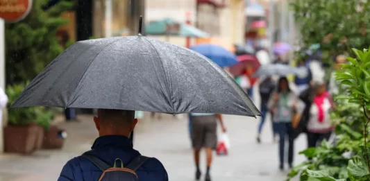 Pessoa caminha com guarda-chuva durante chuva em área urbana, ilustrando a previsão de chuva frequente em Santa Catarina nos próximos três meses.