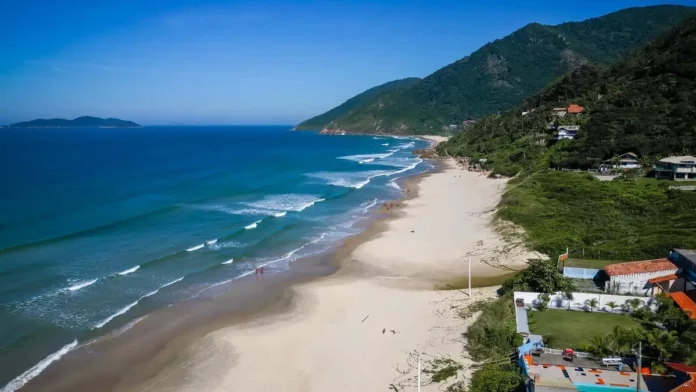 Vista aérea da Praia dos Açores, em Florianópolis, com faixa de areia, mar azul e morros cobertos por vegetação, uma das praias que conquistaram a certificação Bandeira Azul para a temporada 2026/2027.