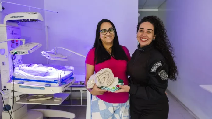Duas mulheres apresentam kits com toucas e cueiros destinados aos recém-nascidos do Hospital Regional de São José, produzidos por internas do sistema prisional catarinense.