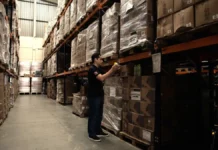 Trabalhador confere produtos armazenados em depósito, ilustrando as compras públicas e o controle de gastos em licitações de Santa Catarina.